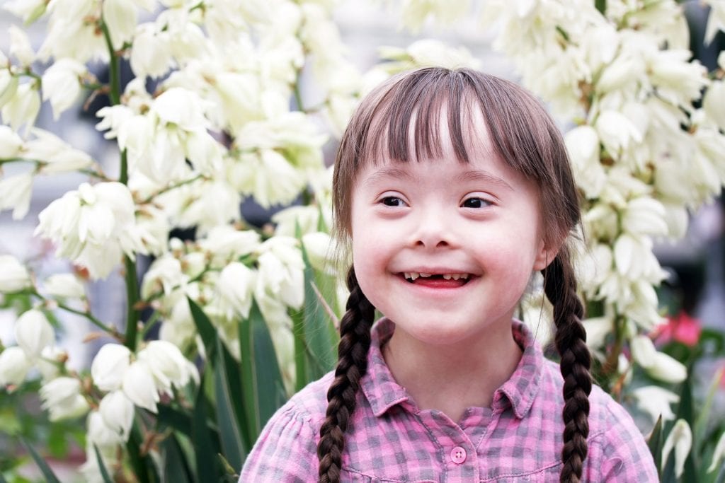 Young girl with down syndrome smiling with white flowers in background