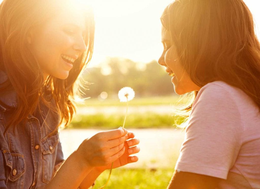 Mother and daughter smiling and blowing on a dandelion.