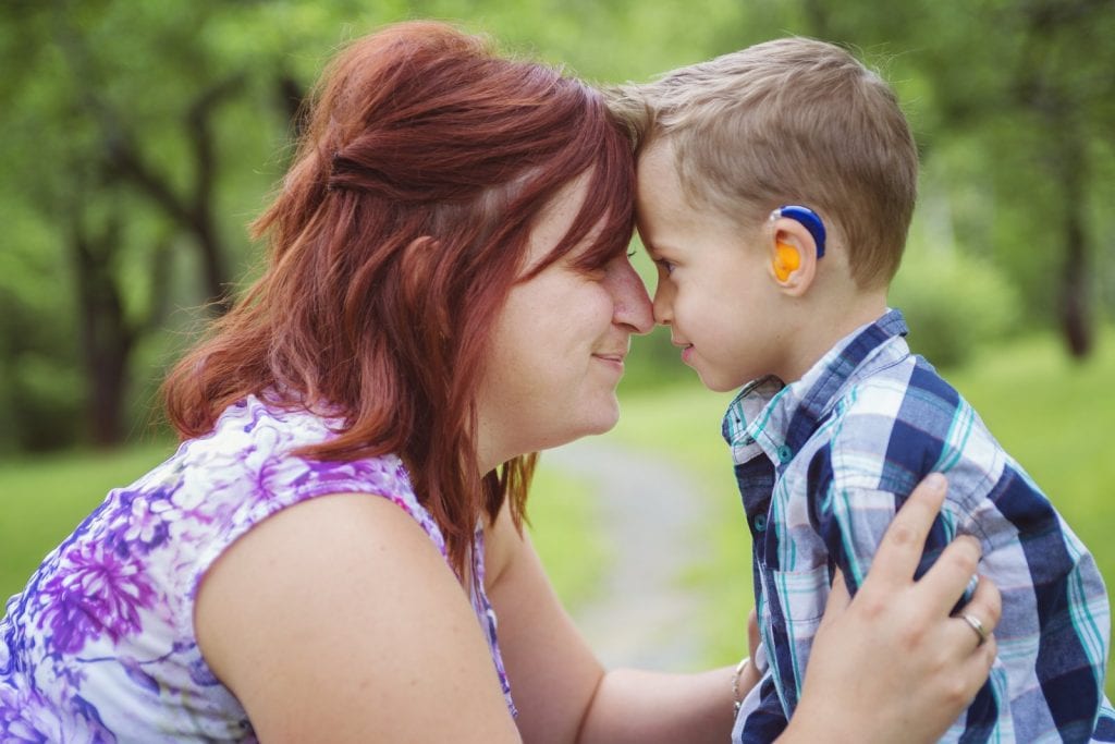 Happy mother and young son with a hearing aid touching noses