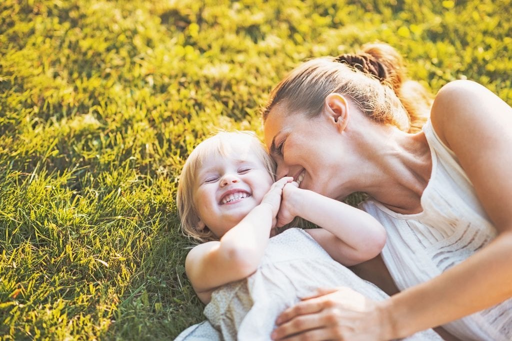 young mother laughing with young toddler daughter lying in grass