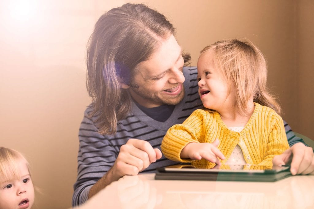 Young father laughing with child with down syndrome playing on an tablet device