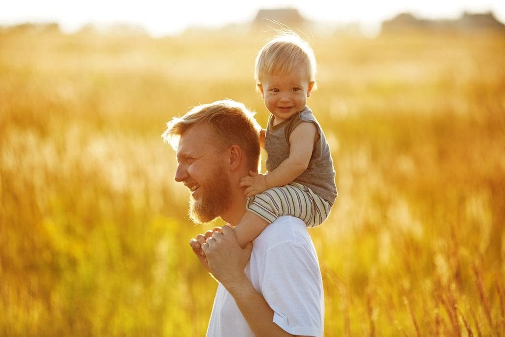 Man standing in field with young toddler on shoulders