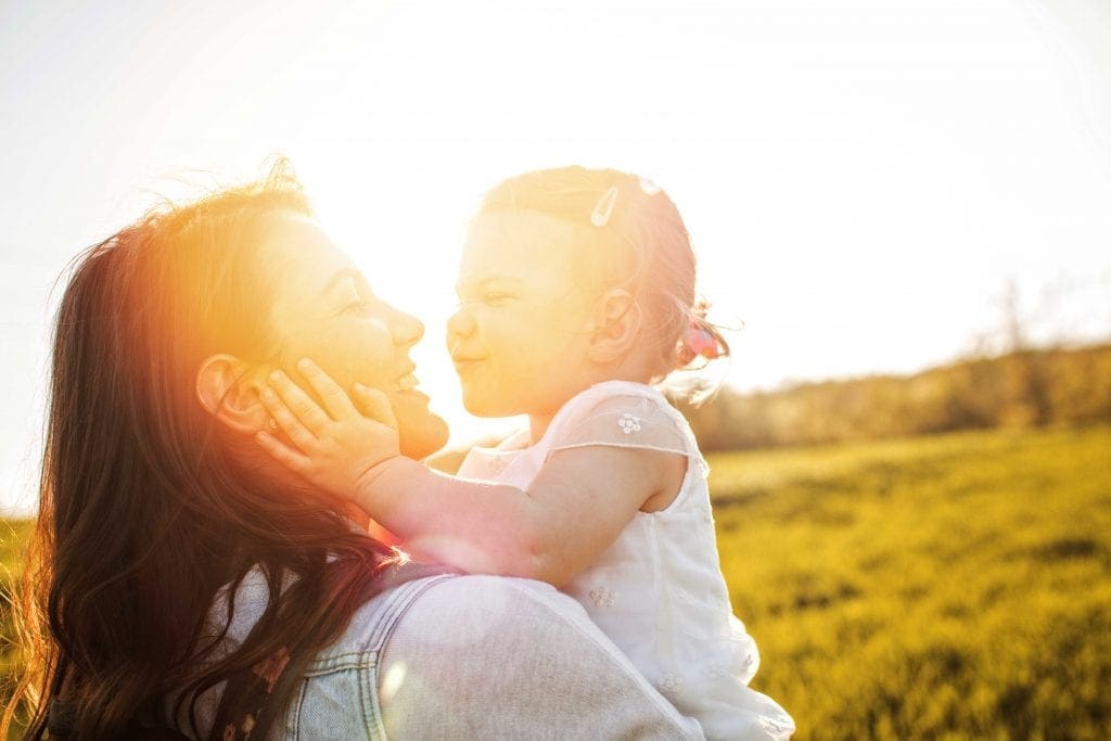 young mother holding toddler daughter and smiling outside
