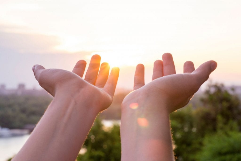 Two hands reaching out with sunshine in background
