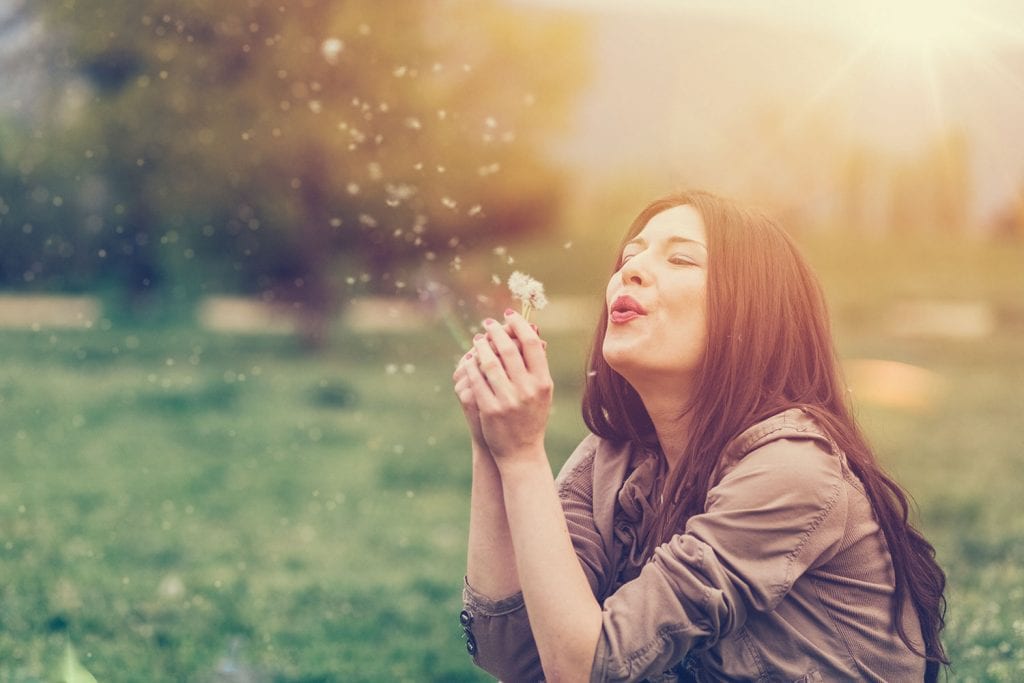 Lady blowing on a dandelion sitting in a park