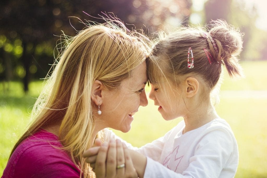 Young mother is hugging her daughter with visual impairment in the park on a sunny day. Genuine emotions, AdobeRGB profile.